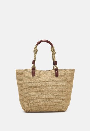 Grand sac fourre-tout tissé beige avec des poignées en corde épaisse torsadée et des accents en cuir marron foncé sur fond blanc.