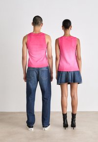 Dwie osoby stoją plecami do siebie, ubrane w dopasowane różowe tank topy w gradient. Jedna z nich łączy go z niebieskimi dżinsami, a druga z dżinsową spódnicą i czarnymi botkami.