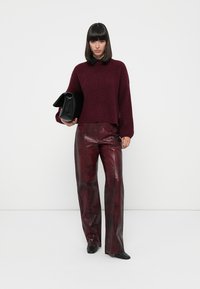 Burgunderfarbener Strickpullover mit Rundhalsausschnitt, kombiniert mit glänzenden burgunderfarbenen Lederhosen im Krokodilmuster und einer schwarzen Handtasche.