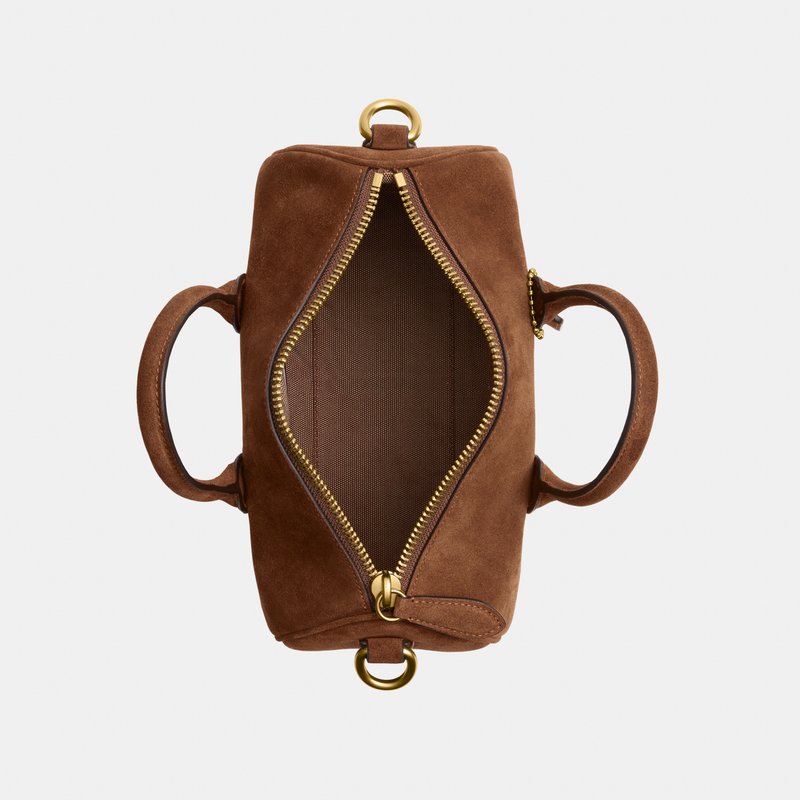 Sac à main en daim marron avec fermeture éclair dorée partiellement ouverte, montrant l'intérieur vide et deux poignées arrondies sur un fond clair.