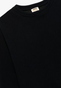 Camisa de manga larga de canalé negra con cuello redondo y una etiqueta de cuidado en el cuello. La tela parece suave y texturizada.