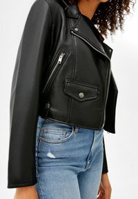 Zwarte nep leren cropped motorjack met zilveren ritsen, zijzakken en een drukknoopsluiting. Gestyleerd met versleten lichtblauwe jeans.