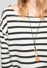 Schwarz-weißer gestreifter Pullover mit weitem Ausschnitt, der eine lange schwarze Halskette mit einem orangefarbenen Anhänger und Details aus Holzringen zeigt.