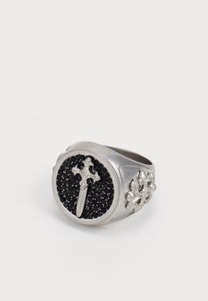 Silver-toned ring with a circular black stone center featuring a cross design, accented with floral motifs on each side.
