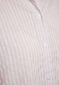 Camicetta button-up di colore viola chiaro con righe verticali bianche, dotata di bottoni in plastica trasparente e una trama liscia e morbida.