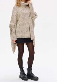 Chunkig beige stickad tröja med hög krage och ribbade ärmar, bärs över en svart denim minikjol och svarta snörade kängor.