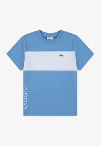 Μπλε κοντομάνικο μπλουζάκι με λευκή οριζόντια ρίγα, μικρό πράσινο λογότυπο κροκόδειλου στο στήθος και το κείμενο "LACOSTE" στο κάτω αριστερό μέρος.