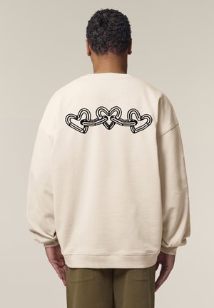 Crème kleur sweatshirt met een losse pasvorm, voorzien van een zwart hartvormig graphic op de achterkant. Geribbelde manchetten en zoomdetails.