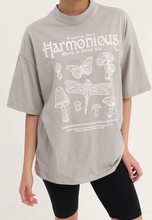 Hellgraues übergroßes T-Shirt mit weißen Illustrationen von Pilzen, Libelle, Schmetterling und Text über das Leben im Wald, getragen mit schwarzen Shorts.