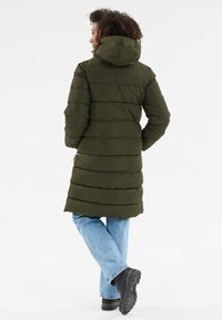 Olivengrøn, pufferjakke med horisontale syninger, hætte og lommer; parret med lyseblå jeans og sorte, strukturerede støvler.