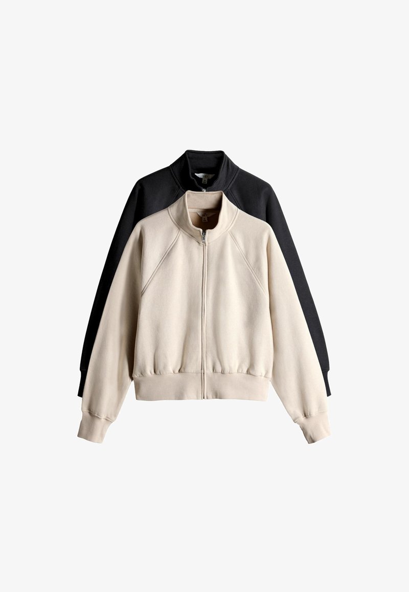 Kaks kokkupandud lukuga pusad kõrgete kraedega, üks beež ees ja üks must taga, valgel taustal.