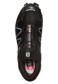 Zapatilla deportiva negra con una superficie texturizada, que presenta una forma estrecha, acentos azules y un logo. Cordones y un cuello acolchado visibles en la parte superior.
