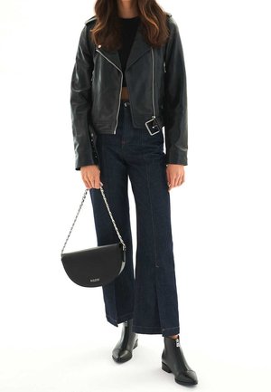Veste de motard en cuir noir avec fermetures éclair argentées, jean large taille haute bleu foncé, sac à main noir à chaîne, et bottines noires.