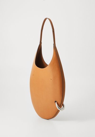 Dzeltenbrūna ādas rokassoma ar ovālu formu, vienu plecu siksnu un sudraba krāsas gredzenu kā izteiksmīgu detaļu. Gluda tekstūra.