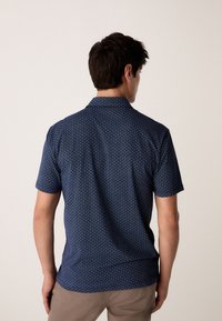 Rövid ujjú, tengerészkék ing geometriai mintával, gallérral és sima textúrával. Hátsó nézet.