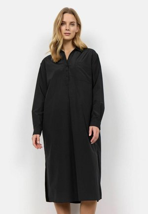 Zwarte jurk met lange mouwen van een gladde stof, voorzien van een kraag, knoopsluiting aan de voorkant, een enkele borstzak en zijspleten aan de onderrand.