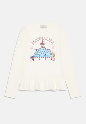 Camisa de manga larga color crema con un gráfico de un sofá tapizado azul, acompañado de un candelabro y una planta en maceta, con un dobladillo con volantes.