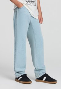 Jeans dritti di colore blu chiaro in denim, con una texture sottile e un classico design a 5 tasche, abbinati a sneakers nere.