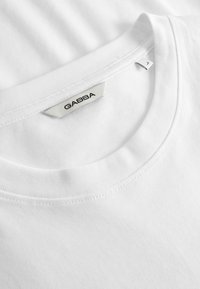 Gros plan sur l'encolure d'un T-shirt en coton blanc avec une étiquette de marque GABBA et une petite étiquette de taille indiquant "L".