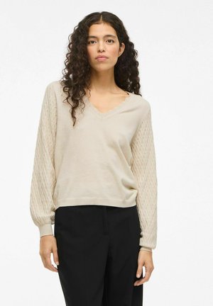 Beige gebreide trui met een V-hals en decoratieve gegolfde rand; textuur, gepatternde mouwen; zachte, lichtgewicht stof; ontspannen pasvorm.