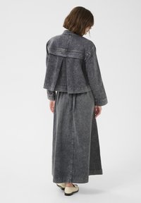 Grå denimjacka med plisserad rygg, matchad med en lös kjol, bärs med ljusfärgade skor. Ren, minimalistisk design.