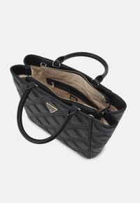 Sac à main noir matelassé avec double poignée, ouverture supérieure dévoilant la doublure intérieure beige, compartiment central zippé et plaque logo Guess sur le devant.