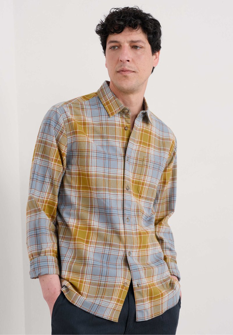 Camisa de cuadros en tonos azul, amarillo y marrón. Presenta mangas largas, cuello con solapa y un bolsillo en la parte frontal. Material de algodón, corte holgado.