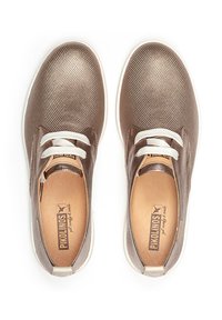 Zapatillas de texturizado bronce con cordones blancos, puntera redonda y suela de goma. Presentan un logo en la plantilla y un diseño liso y elegante.