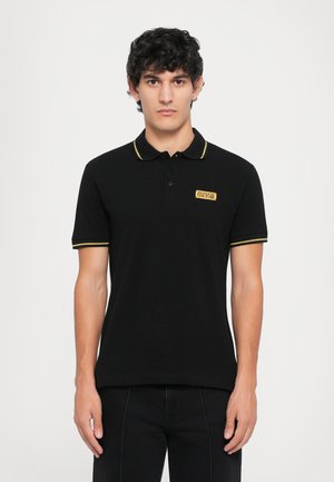 Zwarte poloshirt met gele accenten op de kraag en mouwen, met een klein merklabel op de linkerborst. Glad textuur van de stof.