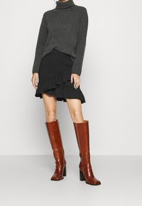 Bottes en cuir marron hautes jusqu'aux genoux avec des talons noirs épais, assorties à un pull à col roulé gris et une jupe noire à volants. Texture lisse, design ajusté.