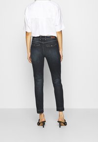 Tummansininen farkkuhousut slim fit -muotoilulla, joissa on takataskut ja vyötärön tagi, yhdistettynä valkoiseen lyhythihaiseen paita.