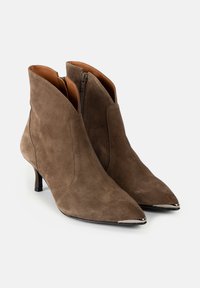Botine din suede maro, cu vârfuri ascuțite, fermoare laterale și accente metalice la vârfuri. Toc subțire și conic adaugă eleganță.