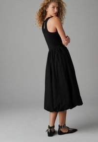 Vestito nero senza maniche con un corpetto aderente e una gonna fluida fino al ginocchio, abbinato a ballerine nere con cinturini alla caviglia e dettagli con fibbia.