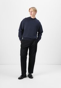 Tengerészpulóver kerek nyakkal, fekete nadrággal és fekete cipővel. Egyszerű dizájn, laza illeszkedéssel és sima textúrával. Minimalista stílus.