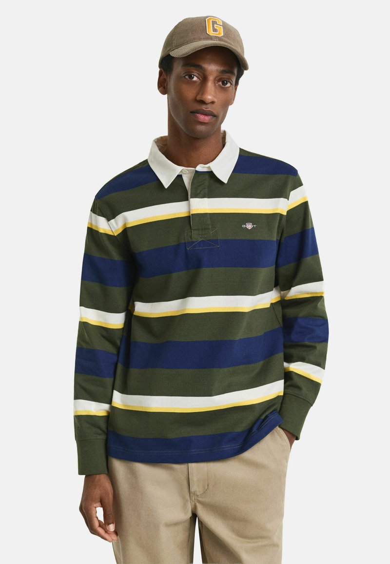Polo de manga larga a rayas en verde, azul marino, blanco y amarillo, con cuello, tapeta de botones y logo en el pecho; combinado con pantalones beige.