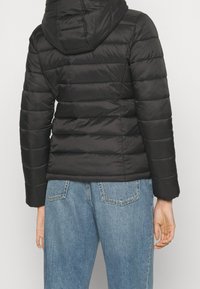 Czarna kurtka puchowa z kapturem, posiadająca pikowany wzór i poziome przeszycia, zestawiona z niebieskimi dżinsami o wysokim stanie.