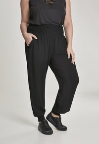 Pantalons noirs légers avec une taille élastique froncée, poches latérales, chevilles effilées, associés à des baskets noires. Texture lisse.