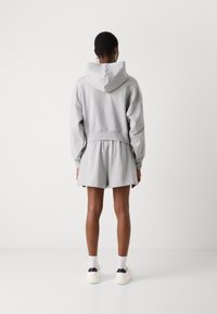 Felpa grigia chiara con cappuccio, design cropped e spalle scese, abbinata a pantaloni corti grigi coordinati. Tessuto uniforme senza motivi visibili.