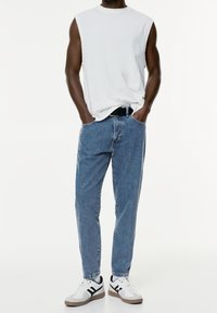 White sleeveless ribbed shirt, light blue straight-leg jeans, black belt, and white sneakers with black accents. Simple and casual design.