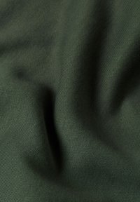 Tejido de color verde oscuro con una textura suave, que presenta un patrón de punto liso y un brillo sutil, cayendo en suaves pliegues.