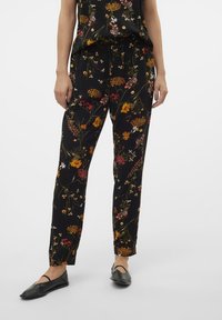 Černé květované kalhoty s šňůrkou v pase, zdobené barevnými květinovými vzory ve žluté, červené a růžové barvě. Měkká látka s volným střihem.