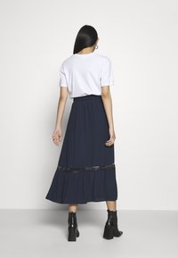 Marinblå maxikjol med ett lager-på-lager nederkant, accentuerad med en spetskant. Matchas med en vit t-shirt och svarta klackstövlar med blockklack.