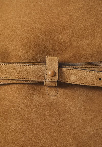 Geantă din suede maro, cu o suprfață texturată, un capac pliabil fixat cu un sistem de închidere tip buton și detalii evidente de cusătură.