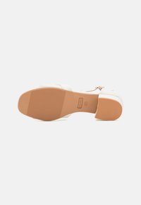 White platform shoes with a smooth leather upper and a textured rubber sole. Notable for their clean design and minimalistic accents.