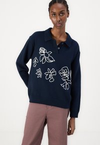 Mornarska majica z belim cvetličnim vezenjem, s ovratnikom in rebrastim robom. Ima tri gumbe pri vratu in ohlapen kroj.