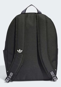 Μαύρος σακίδιο πλάτης με δύο ρυθμιζόμενες straps, χερούλι στην κορυφή, πλαϊνές τσέπες και λευκό λογότυπο στο μπροστινό μέρος. Κατασκευασμένο από υλικό με υφή.