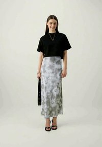 Μαύρο κοντό t-shirt, γκρίζα φλοράλ μαξι φούστα, διαφανές ύφασμα. Μοντέλο κρατώντας μια μαύρη τσάντα, φορώντας μαύρα σανδάλια με λουριά.