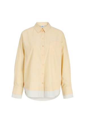 Chemise à manches longues beige clair avec col pointu, poche poitrine, et ourlet et poignets blancs sur fond uni.