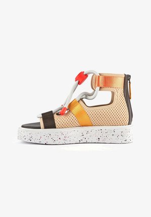 Sandalia ligera con parte superior de malla beige, con correas negras, naranjas y grises. Suela blanca gruesa moteada, con cierre de cordones y cremallera.