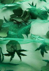 Grünes Netzgewebe mit kunstvollen botanischen Motiven, das überlagerte Blumen-Applikationen und Blattmuster in verschiedenen Grüntönen aufweist.